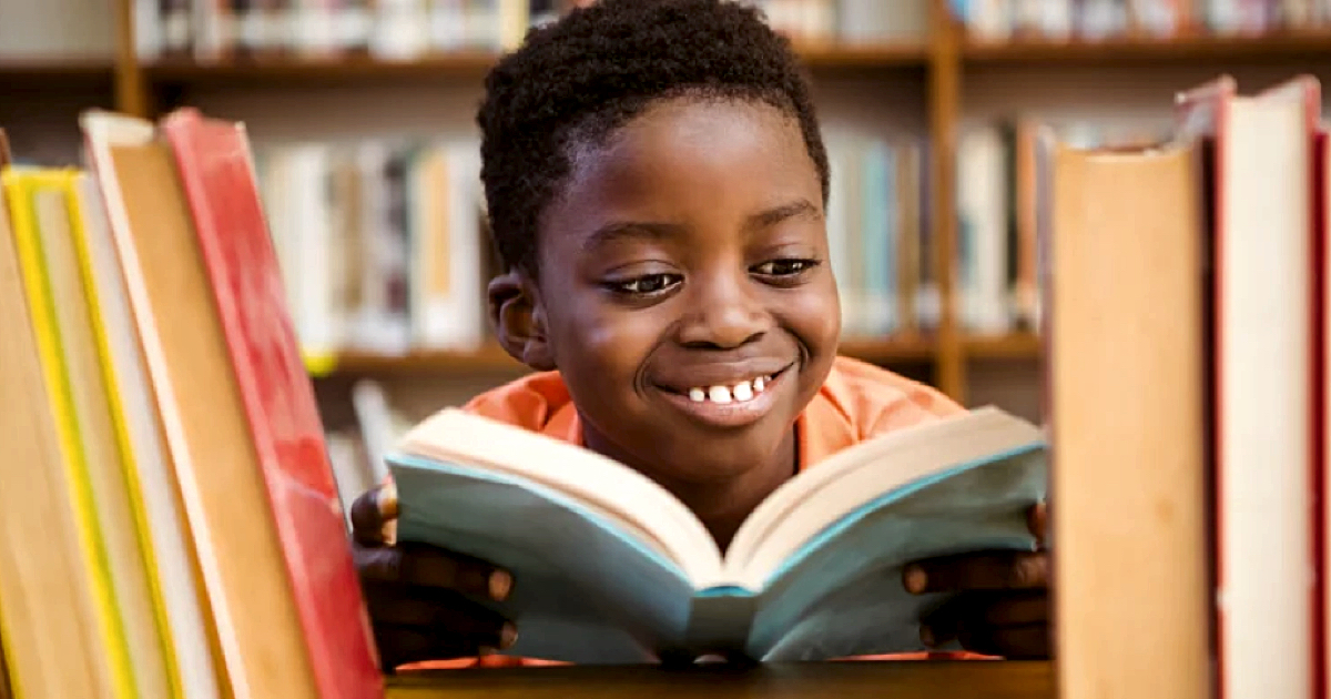 Cute Black boy reading a book in a library
